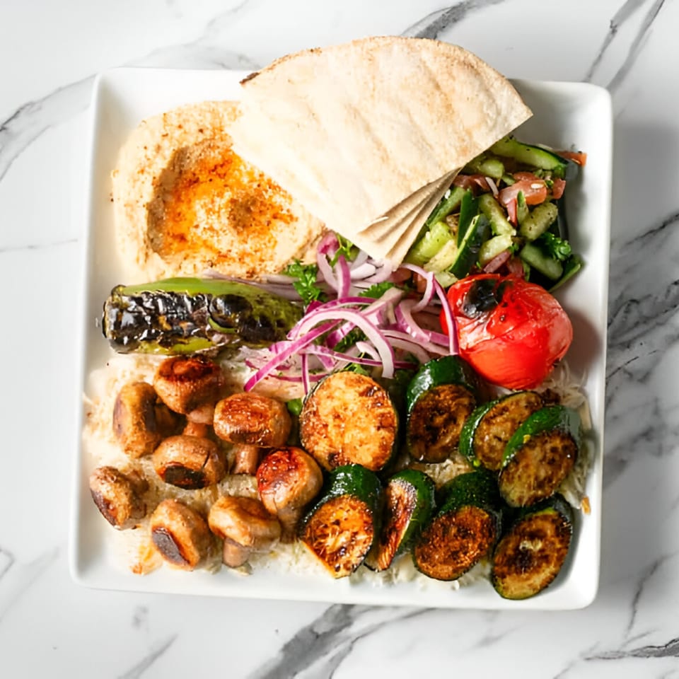 Mediterranean platter with hummus, pita, cucumber salad, grilled vegetables, and mushrooms on a white plate.