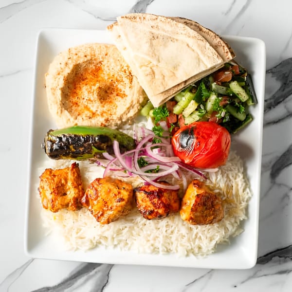 Sepan Chicken plate with chicken skewers, rice, hummus, pita bread, salad, grilled tomato, and pepper.