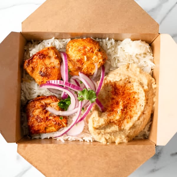Sepan Chicken's Mediterranean chicken and hummus plate with rice, red onions, and parsley in a to-go box.