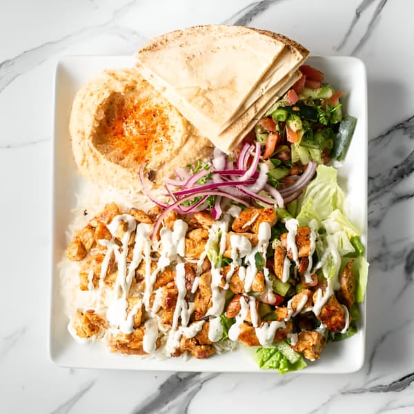 Sepan Chicken plate with chicken, rice, hummus, pita, salad, and red onions on marble.