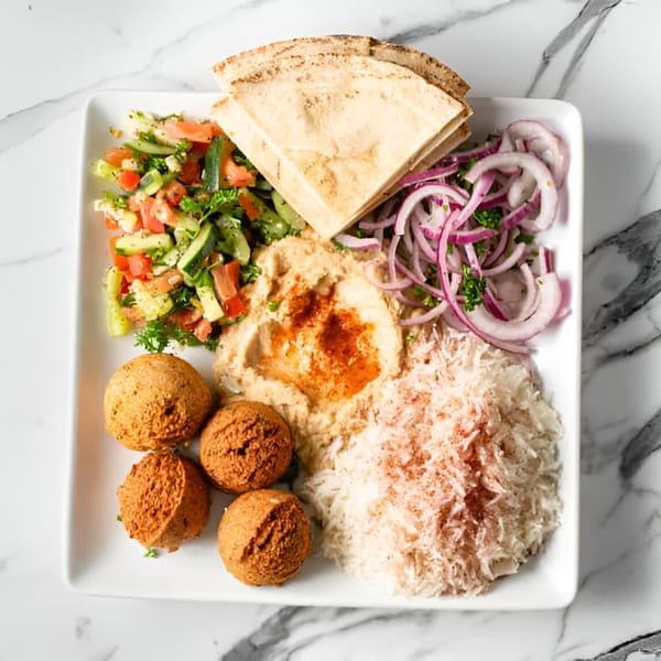 A white plate with falafel, hummus, salad, rice, red onions, and pita bread on a marble surface.